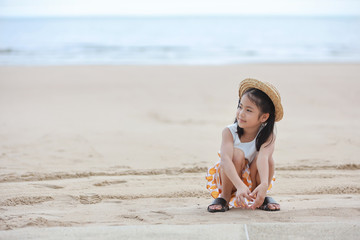 happy asian little girl with nice hat playing sand on sandy beach with happy smiling face