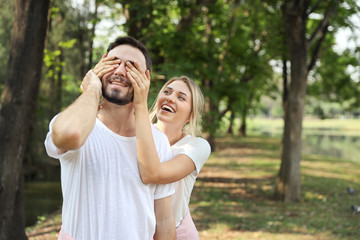 medium shot, young lovely couple caucasian in white dress playing blindfolded with happy face and laughing in park outdoor during summer
