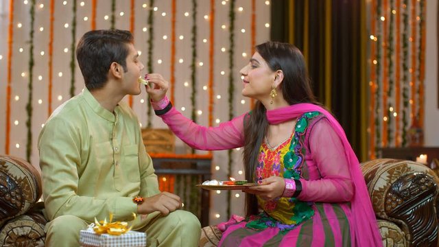 Young brother and sister eating sweets and celebrating Raksha Bandhan festival. Beautiful sister offering sweets to her brother on this special occasion  Rakhi festival - showing love for each other