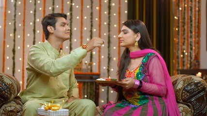 Naughty Indian brother happily teasing her sister on the special occasion of Raksha Bandhan. Young cute brother and sister fighting and teasing each other over sweets - enjoying rakhi  sharing sweets