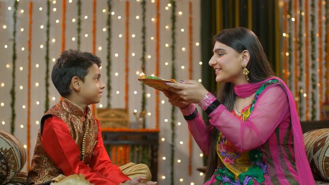 Young Indians happily performing Raksha Bandhan / Bhai Dooj traditions. Pretty elder sister celebrating Raksha Bandhan / Bhai Dooj rituals of doing aarti / pooja of her sweet little brother