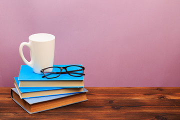  pile of old books with mug ang glasses  panorma, good copy space  on pink background