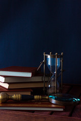 BOOKS ALONG TO CLOCK OF SAND AND MAGNIFYING ON WOODEN TABLE