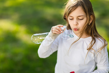 young girl blowing soap bubbles in park