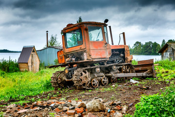 Old dirty tractor by the river in a rustic landscape.