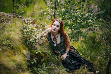 A forest witch. A beautiful girl lies on a moss in a beautiful wreath and a green dress. Moss on the ground.