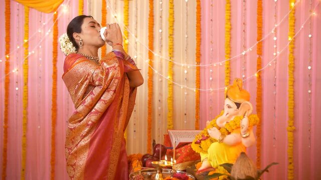 Young Indian woman dressed in traditional saree and blowing the sankha (counch shell) for Ganesh pooja. HD stock video of an attractive young newly married woman performing puja at her new home 