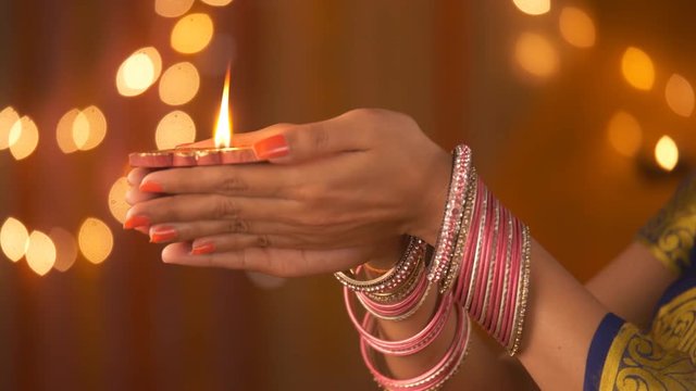 Beautiful hands of an Indian woman wearing bangles - holding a diya. Diwali Festival. Indian stock footage of daughter-in-law of the family lighting a diya and holding with both hands