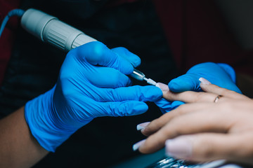 Fototapeta na wymiar Manicurist. A girl with blue gloves makes a manicure. The process of manicure.