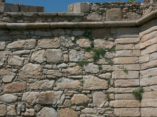 Old, rough, exterior stone wall of Portuguese castle with grass growing in cracks