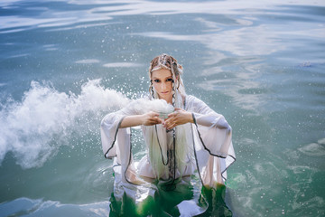 Elf girl in white dress in water. The model in a medieval dress with pigtails keeps a bowl of smoke.