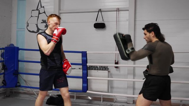 Boxer man kicking boxing pad while personal training with coach. Man fighter in boxing gloves punching pad. Personal trainer training boxer. MMA K1 martial arts