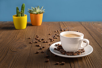 A coffee cup with coffee beans on a wooden table with colorful flowerpots, selective focus