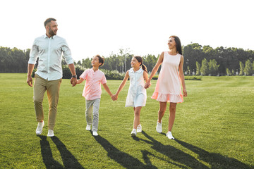 I love my family Full length of happy and young family of four holding hands, smiling and walking...