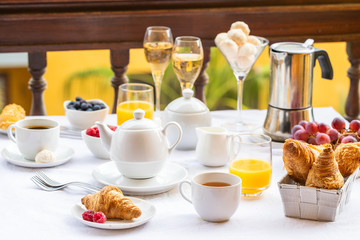 Luxury brunch on the hotel  terrace, coffee maker, teapot, cups, croissants, fruits, orange juice and champagne. Good morning scenery background.