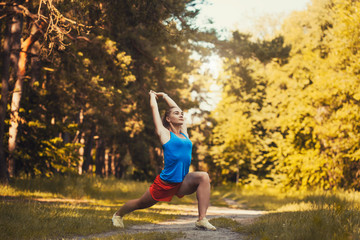 Pretty woman athlete doing exercises before jogging through the summer forest