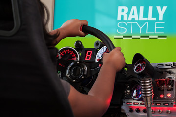 A girl playing a rally game holding a steering wheel from a racing sim cockpit and turning the...