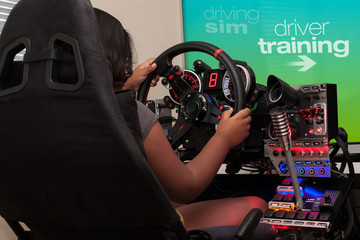 A young person sitting in a racing cockpit and selecting driver training from the gaming screen while holding the steering wheel.