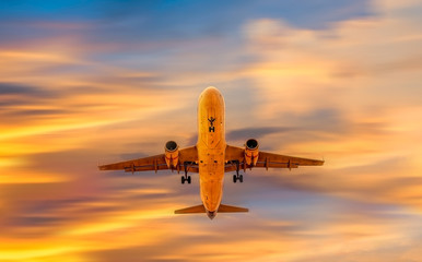 Airplane flying above dramatic clouds during sunset sky