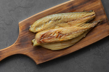 Raw smoked mackerel fillets on a rustic wooden chopping board.  With a grey tile background
