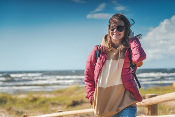 Young happy beautiful girl walks along the cold shore of the Baltic Sea in windy sunny weather, traveling to the Scandinavian countries