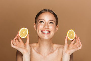 Beautiful happy young amazing woman posing isolated over brown chocolate background wall holding lemon.