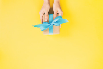 Woman arms holding gift box with blue ribbon on color background, top view