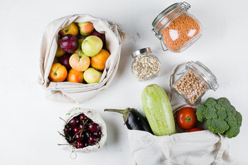 Zero Waste Food Storage Eco Bag Top View. Reusable cotton bag with fresh vegerables, fruits, berry, glass jar with cropus on white stone table background. Top view, flat lay, copy space