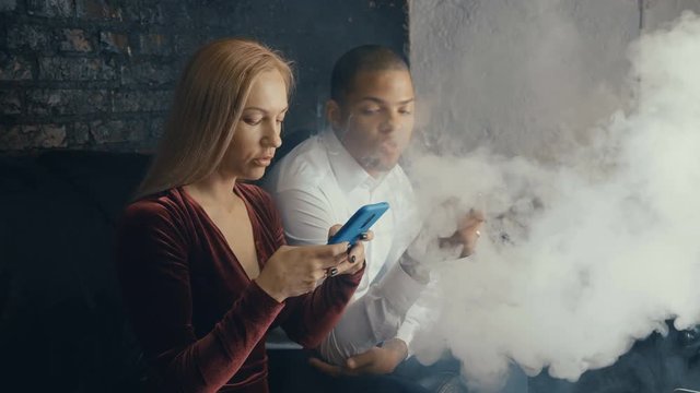 Multiracial couple talking in coffee house, man smoking vape and woman drinking coffee in restoraunt, diverse people negotiating at meeting in cafe