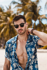 Handsome mature male model enjoying a sunny day on the beautiful island of Boracay. Walking with open blue shirt between palm trees on famous white beach.