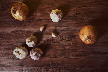  Photograph of garlic and onions on a brown wooden table.