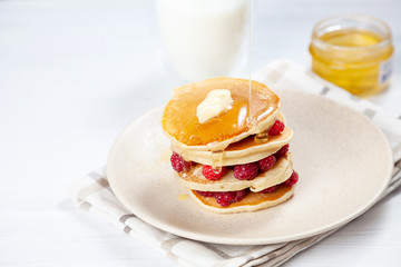 Closeup on stack of fresh, homemade pancake stack with raspberry, melting butter and pouring honey or marple syrup. american pancake on white background with morning light. Breakfast. selective focus.