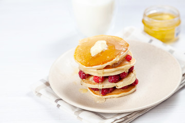 Closeup on stack of fresh, homemade pancake stack with raspberry, melting butter and pouring honey or marple syrup. american pancake on white background with morning light. Breakfast. selective focus.