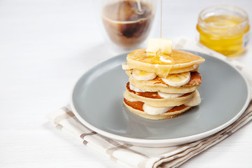 Closeup on fresh, homemade pancake stack with banana, melting butter and pouring honey or marple syrup. american pancake with glass of coffee with morning light. Breakfast food with copy space