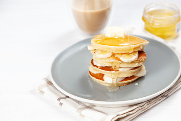 Closeup on fresh, homemade pancake stack with banana, melting butter and pouring honey or marple syrup. american pancake with glass of coffee with morning light. Breakfast food with copy space