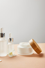 Obraz na płótnie Canvas cosmetic glass bottles, open jar with cream and jasmine flower on beige