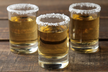 Gold tequila in a glass with salt and lime on a brown wooden table. alcoholic beverages.