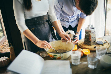 Young couple cuddling their golden retriever dog in front of the table while cooking together.