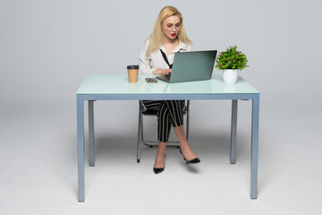 Smiling business woman sitting by the table with laptop and looking at camera in office