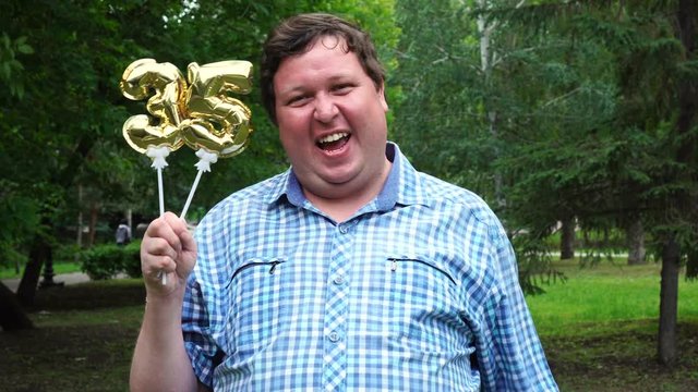 Big man holding golden balloons making the 35 number outdoor. 35th anniversary celebration party