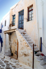 One of the charms of Mykonos, Greek island in the heart of the Cyclades, are its narrow staircases to access white houses with small flowered balconies touching almost above the cobblestone streets