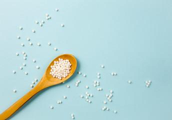 Selective focus on wooden spoon with small white round homeopathy pills against blue background, tiny pills scattered around. Border, copy paste.