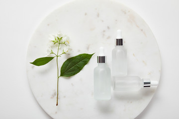 top view of plate with jasmine and cosmetic glass bottles on white surface