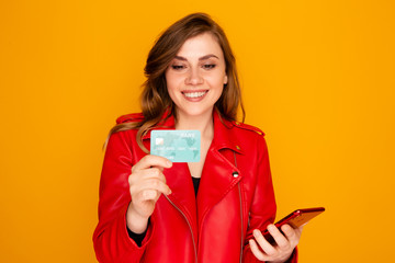 Naklejka premium Happy young woman holding credit card on standing on the yellow background
