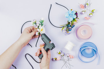 Close-up of woman's hand sticking the flowers on hairband with electric hot glue gun on white...