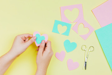 Woman's hand making heart shape with blue and pink paper on yellow background