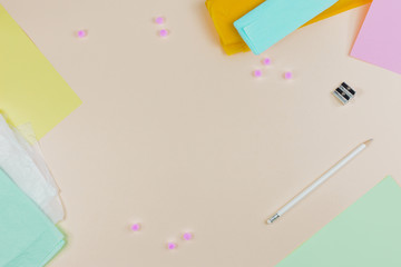 An overhead view of colorful papers with sharpener and white pencil on beige background