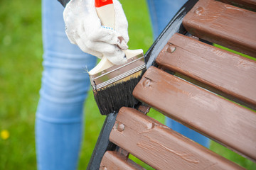 Girl paints a bench in the park. Work with paint. Time to upgrade the garden. Girl with a brush in...