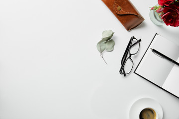 top view of notepad, pen, glasses, case, plants and coffee on white surface