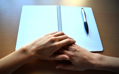 Folded Hands and a White Lined Notebook on a Desk 1 - obrazy, fototapety, plakaty